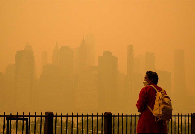 A man with backpack standing beside a fence with smoke foggy city in the background