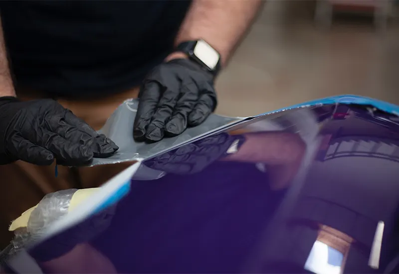 A paint booth technician is applying chemical on the surface of a purple car